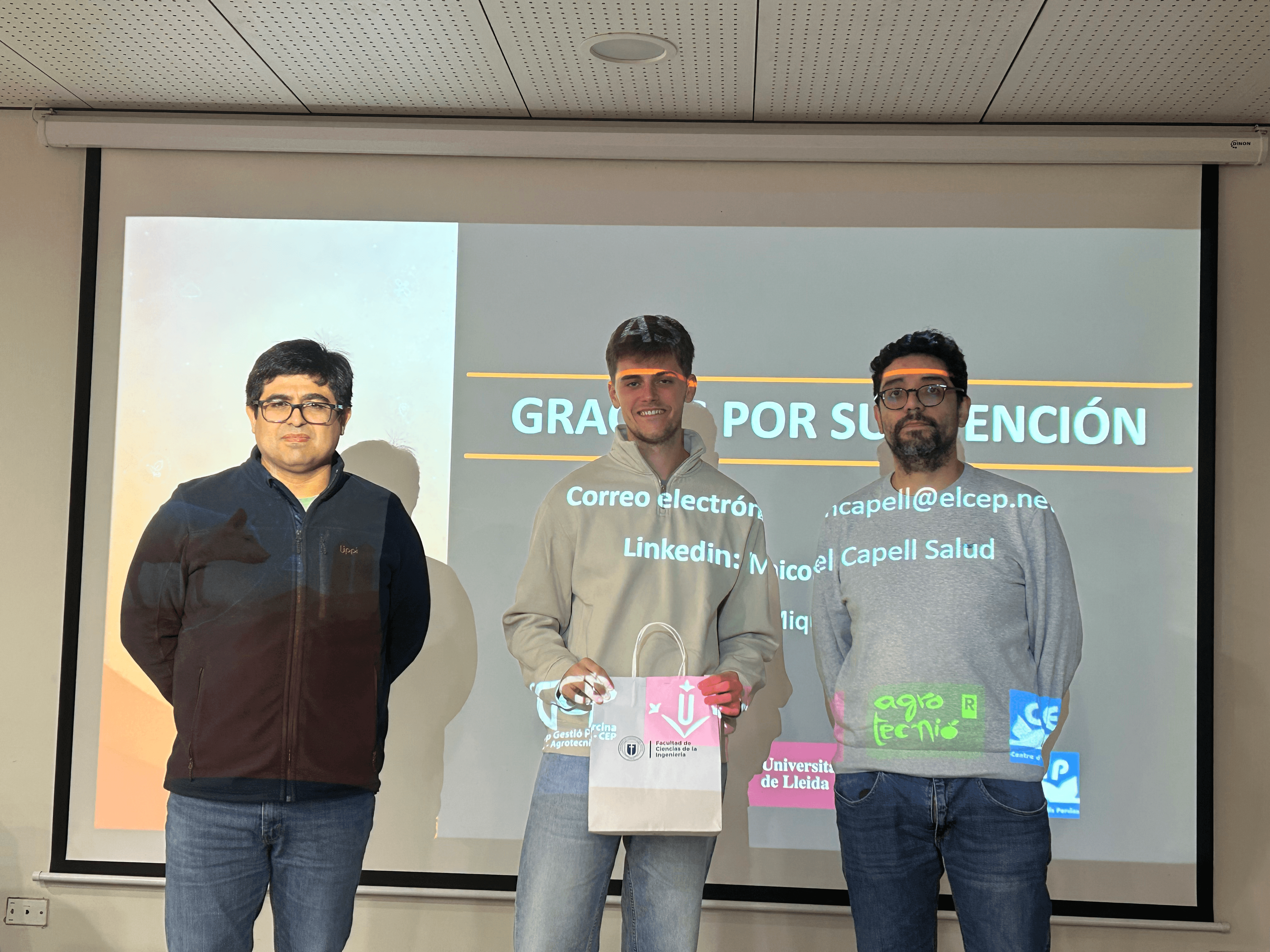 Tres hombres posando juntos en un evento de presentación en la universidad.