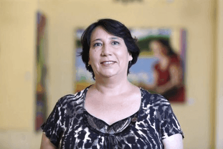 Una mujer sonriente posa frente a un fondo artístico en un ambiente acogedor.