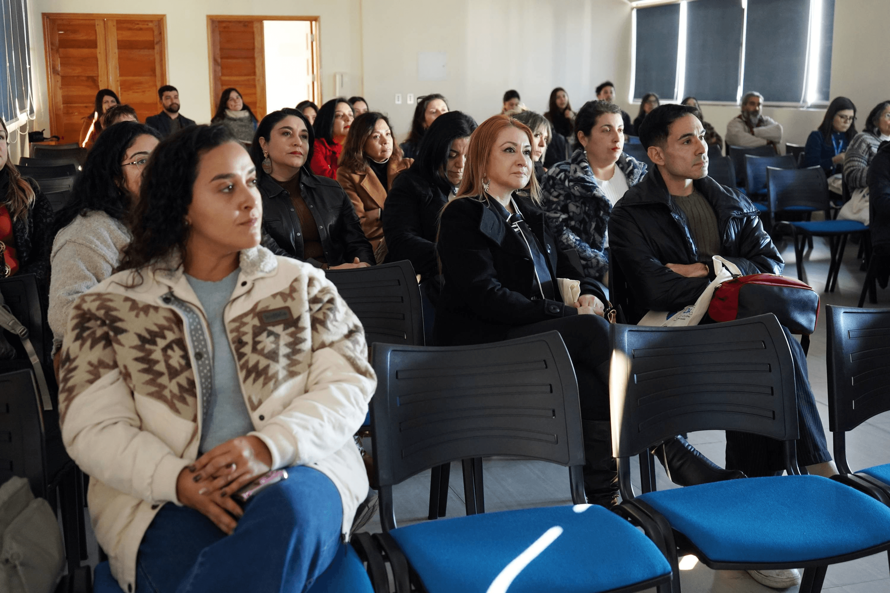 Un grupo de personas sentadas en una sala prestando atención a una presentación.