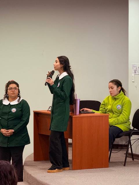 Tres estudiantes presentan un proyecto en un aula.