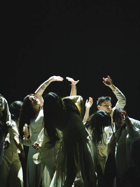 Un grupo de personas danza en un escenario oscuro, expresando emociones con movimientos fluidos.