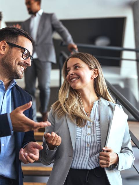 Un par de profesionales conversando amigablemente mientras suben las escaleras en una oficina moderna.