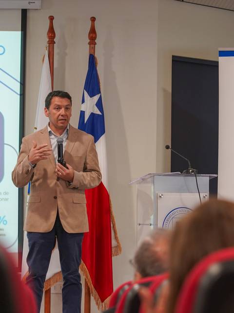 Un expositor presenta un tema en una conferencia en Chile, frente a una audiencia sentada.