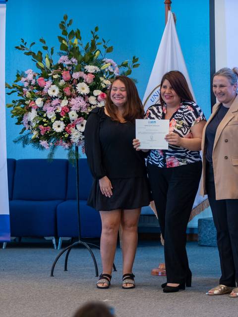 En la imagen, tres mujeres posan juntas durante una ceremonia de entrega de certificados en un evento educativo.