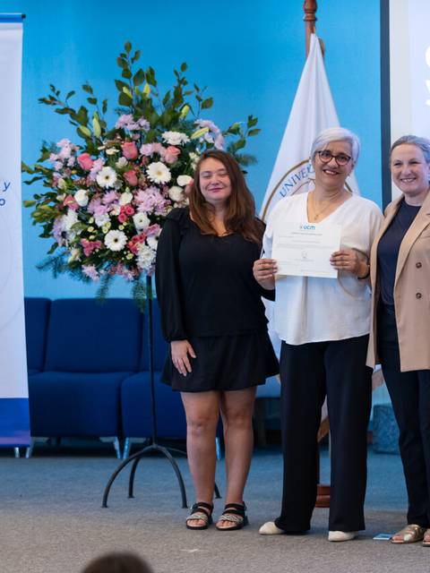 Ceremonia de entrega de certificado en la universidad con flores de fondo.