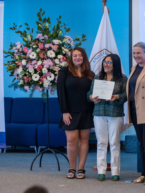 Una ceremonia en la que tres mujeres posan con un certificado en un ambiente académico.