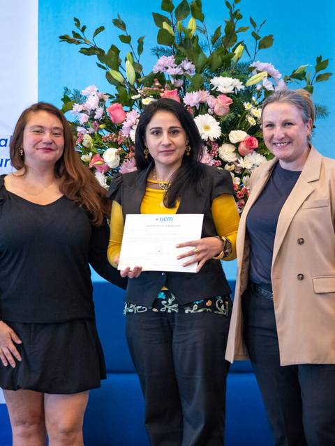 Tres mujeres posando con un certificado en una ceremonia de entrega en la universidad.