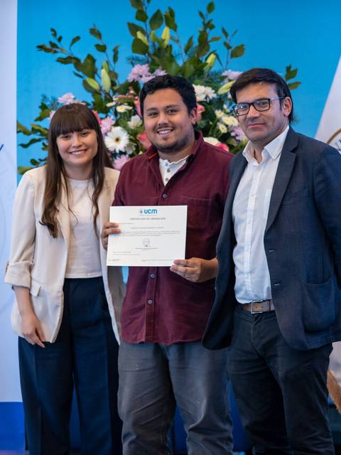 Un grupo de tres personas sonríe mientras sostienen un certificado en un evento académico.