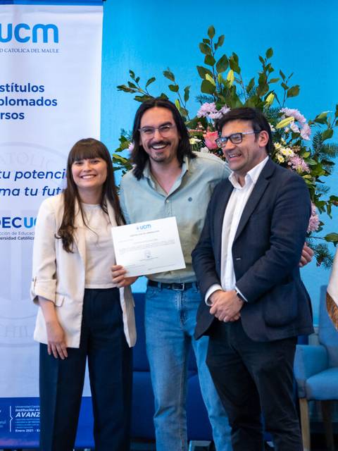 Un grupo de tres personas sonríen mientras sostienen un certificado en un evento de graduación.