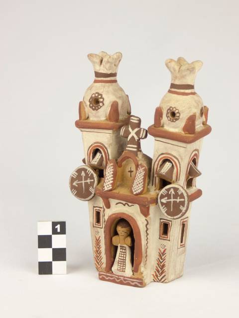 Escultura de cerámica que representa una construcción con torres y una figura en la entrada.