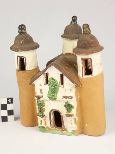 Una cerámica en forma de castillo con domos, decorada con detalles verdes y una puerta central.