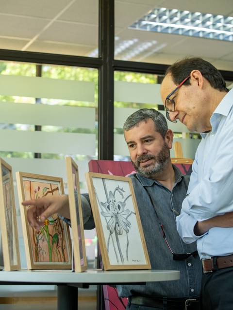 Dos hombres observan atentamente obras de arte en una exposición.