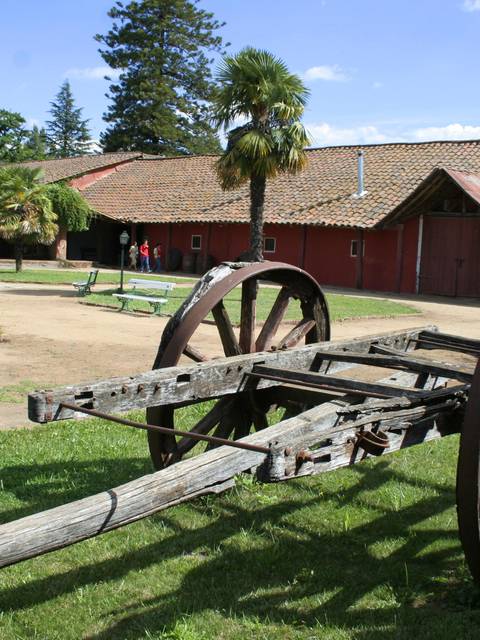 Un carro de madera antiguo se encuentra en un paisaje verde junto a un edificio de estilo rústico.
