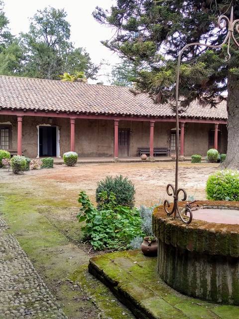 El patio de un edificio antiguo con un pozo y vegetación alrededor.