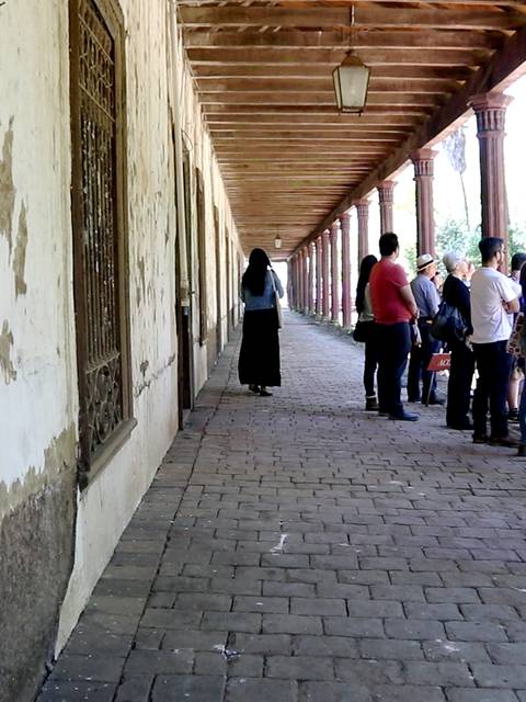 Una fila de personas esperando en un pasillo antiguo con muros desgastados.