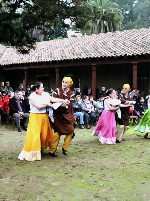Un grupo de bailarinas tradicionales danzan en un espacio al aire libre mientras son observadas por un público entusiasta.