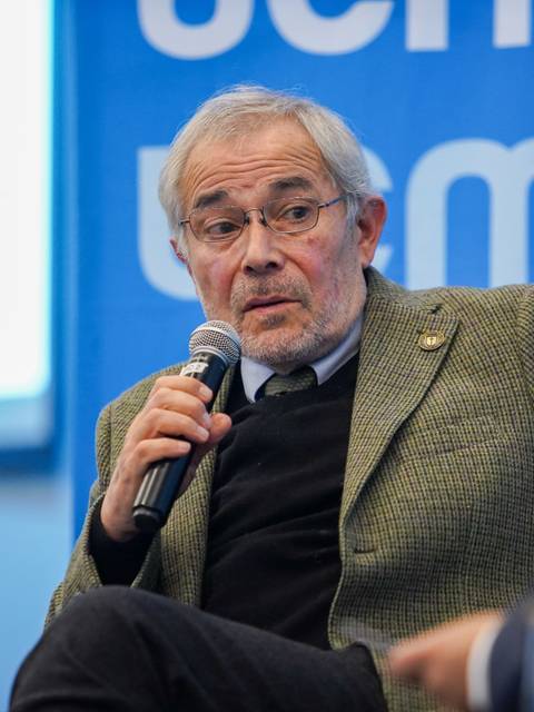 Un hombre mayor con gafas habla en un panel de discusión.
