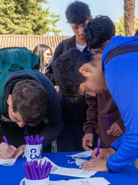 Un grupo de jóvenes en un evento, escribiendo sobre hojas en una mesa.