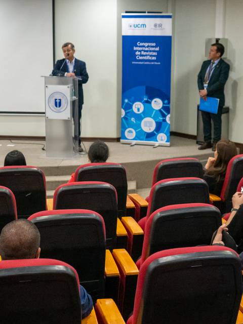 Un evento académico se está llevando a cabo con un orador en el podio y un público atento.