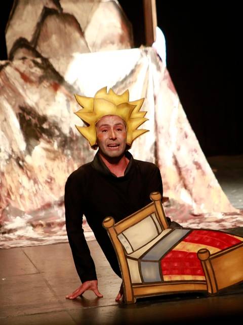 Un actor presenta una obra de teatro con un sombrero de personaje animado y un accesorio de cama.