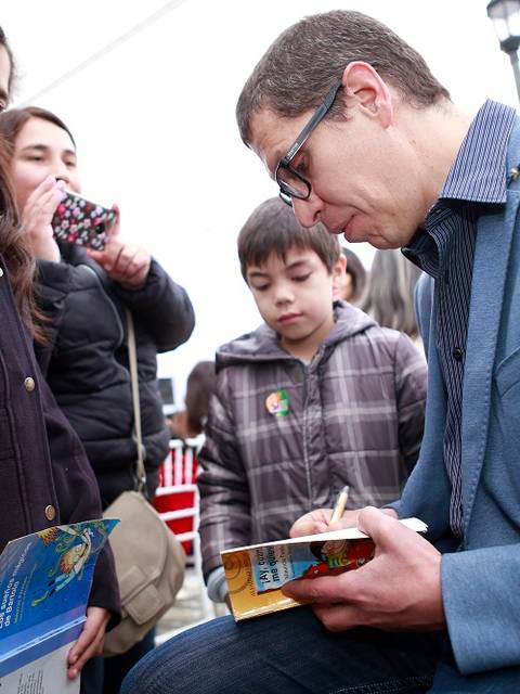Un autor firma libros para un grupo de niños en un evento literario.