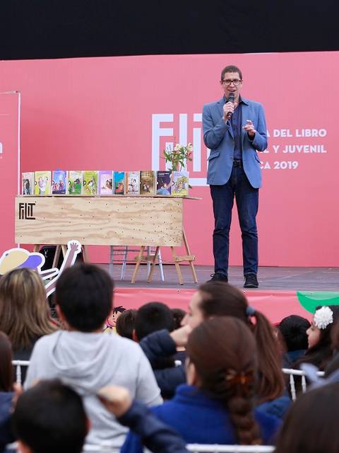 Un presentador habla en un evento literario frente a un público infantil y juvenil.