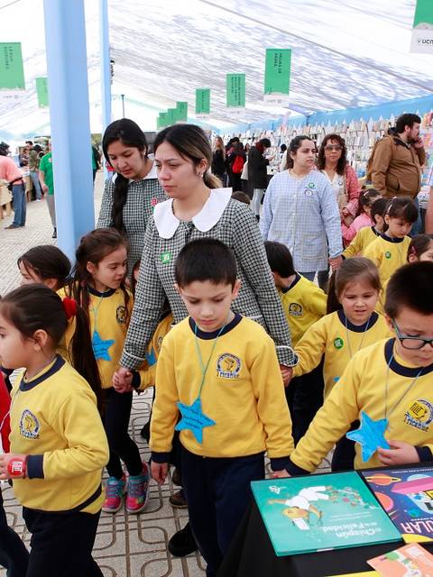 Un grupo de niños en uniforme amarillos camina por un evento literario rodeado de adultos y libros.