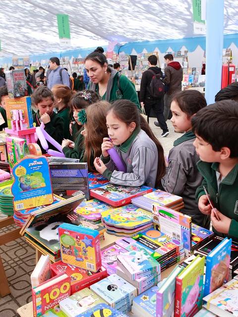 Un grupo de niños observa y elige juguetes mientras un hombre les explica sobre los productos en una feria.