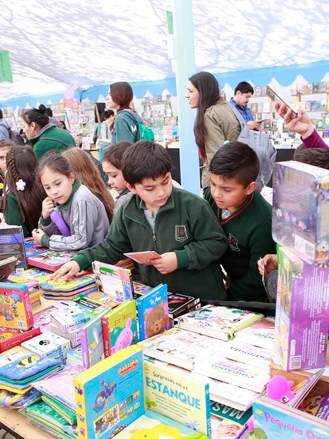 Un grupo de niños y adultos disfrutando de un evento con mesas llenas de juegos y juguetes.