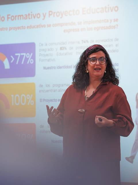 Una profesora presenta información sobre un proyecto educativo a un grupo de personas.