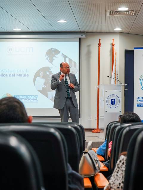 Un expositor disertando frente a una audiencia en un evento académico en la Universidad Católica del Maule.