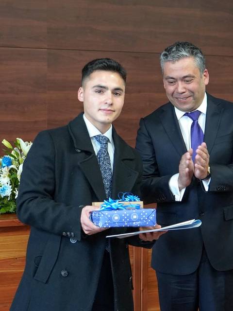 Un joven recibe un premio de mano de un hombre vestido de traje en un evento formal.