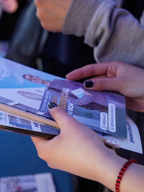 Una persona sostiene un teléfono y una carpeta con información en un evento.