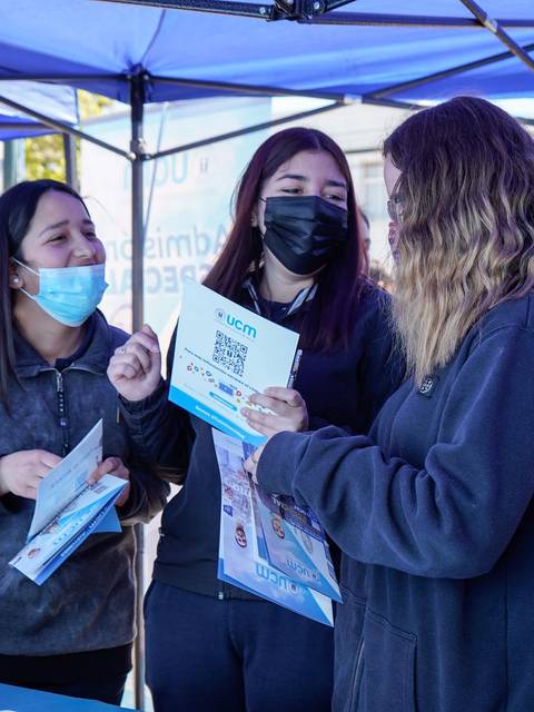 Un grupo de jóvenes conversando y compartiendo folletos debajo de una carpa en un evento al aire libre.