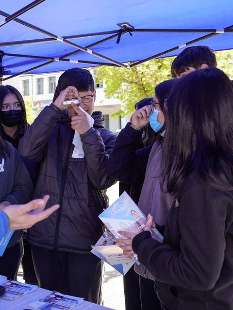 Un grupo de jóvenes interactúa con un presentador bajo una carpa mientras sostienen folletos en un evento al aire libre.