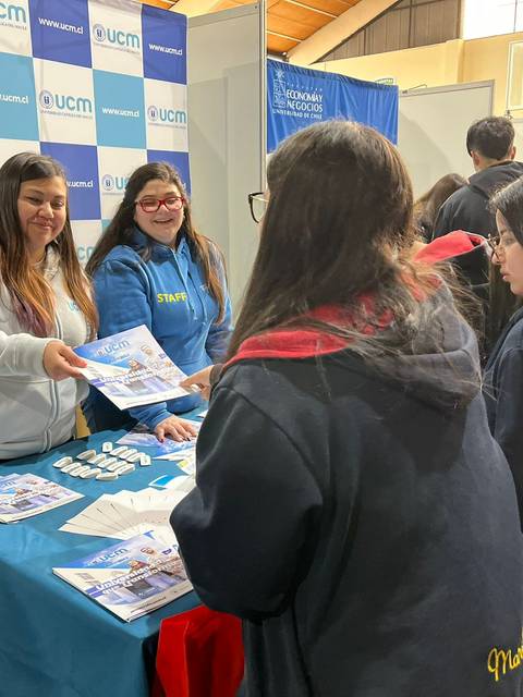 Un grupo de personas interactúa en un stand informativo de la universidad, recibiendo folletos y material promocional.