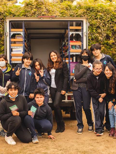 Un grupo de niños y adultos sonríen frente a un camión que parece estar proporcionando libros.