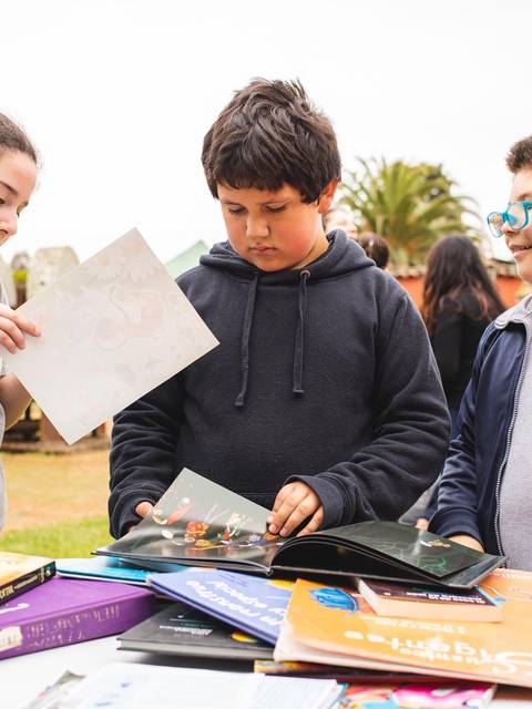 Tres niños revisan libros en un evento al aire libre.