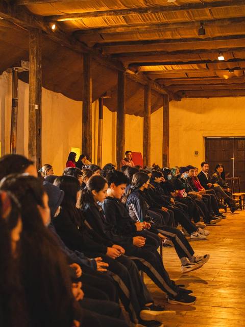 Un grupo de estudiantes escucha a un ponente en un salón con vigas de madera.