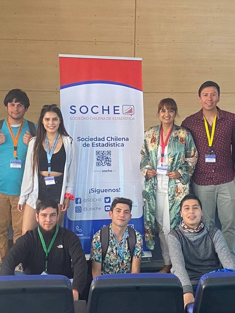 Grupo de personas posando frente a un banner de la Sociedad Chilena de Estadística.