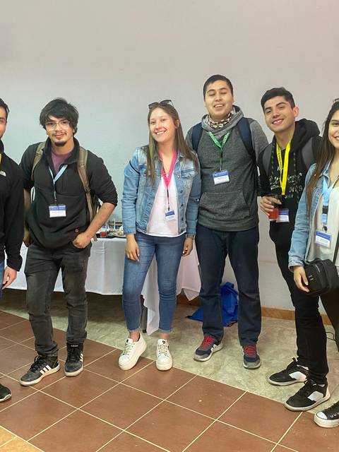 Un grupo de seis personas sonriendo y posando en un evento, todos con identificadores y vestimenta casual.