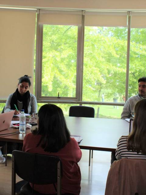 Un grupo de personas se reúne en una sala de trabajo con grandes ventanas que dan a un jardín verde.