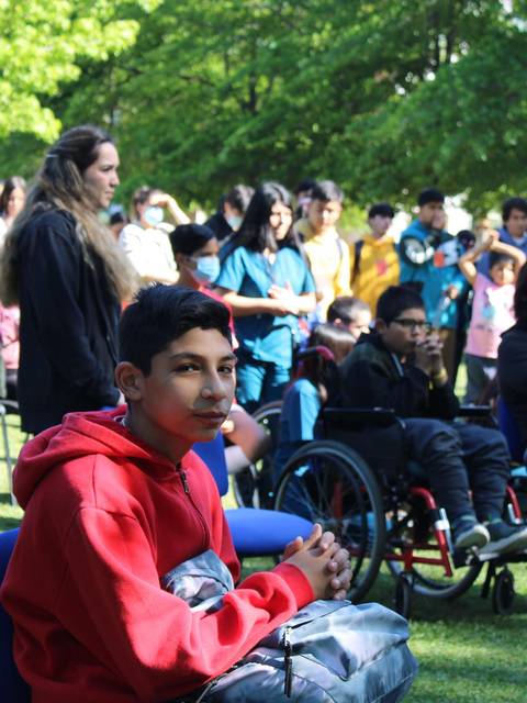 Un grupo de jóvenes en un evento al aire libre, algunos con sillas de ruedas, disfrutan de la actividad mientras una persona en primer plano observa atentamente.
