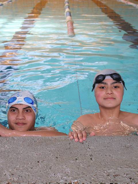 Dos jóvenes nadadores posan en piscina, uno con gorro y gafas de natación.