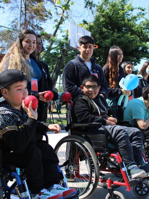 Un grupo de niños y adolescentes participando en una actividad al aire libre, algunos en sillas de ruedas.