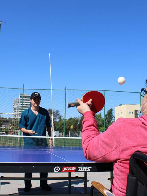 Un grupo de jóvenes juega al ping pong al aire libre en un día soleado.