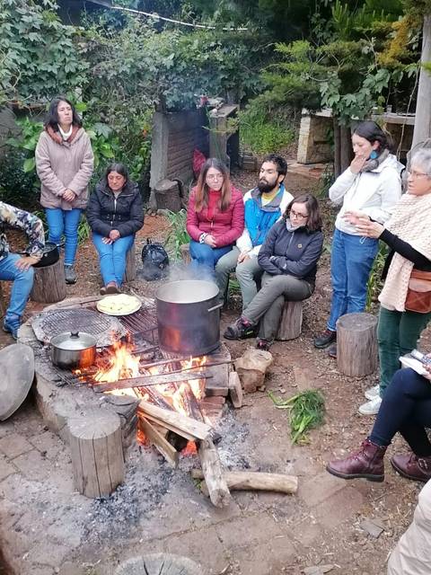 Un grupo de personas se reúne alrededor de una fogata en un ambiente natural para compartir y cocinar.
