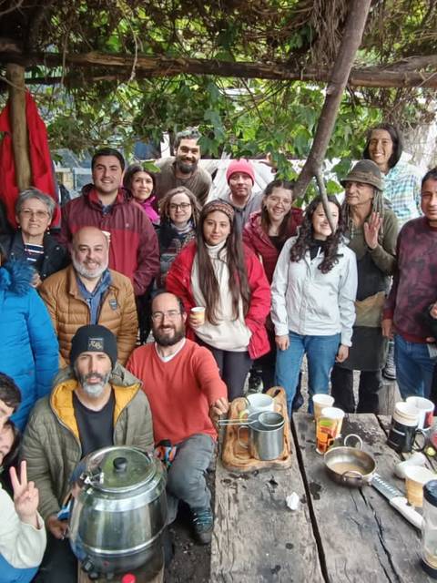 Un grupo de personas sonrientes se reúne en un espacio al aire libre bajo una estructura de madera, disfrutando de un ambiente de camaradería.