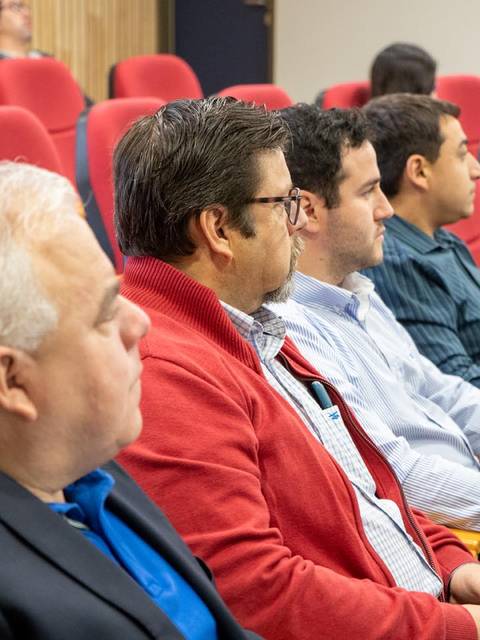 Un grupo de cuatro hombres sentado en sillas rojas en un ambiente de sala de conferencias.