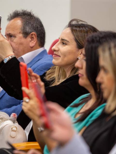 Un grupo de personas sentadas en una sala, algunas usando sus teléfonos móviles para tomar fotos.